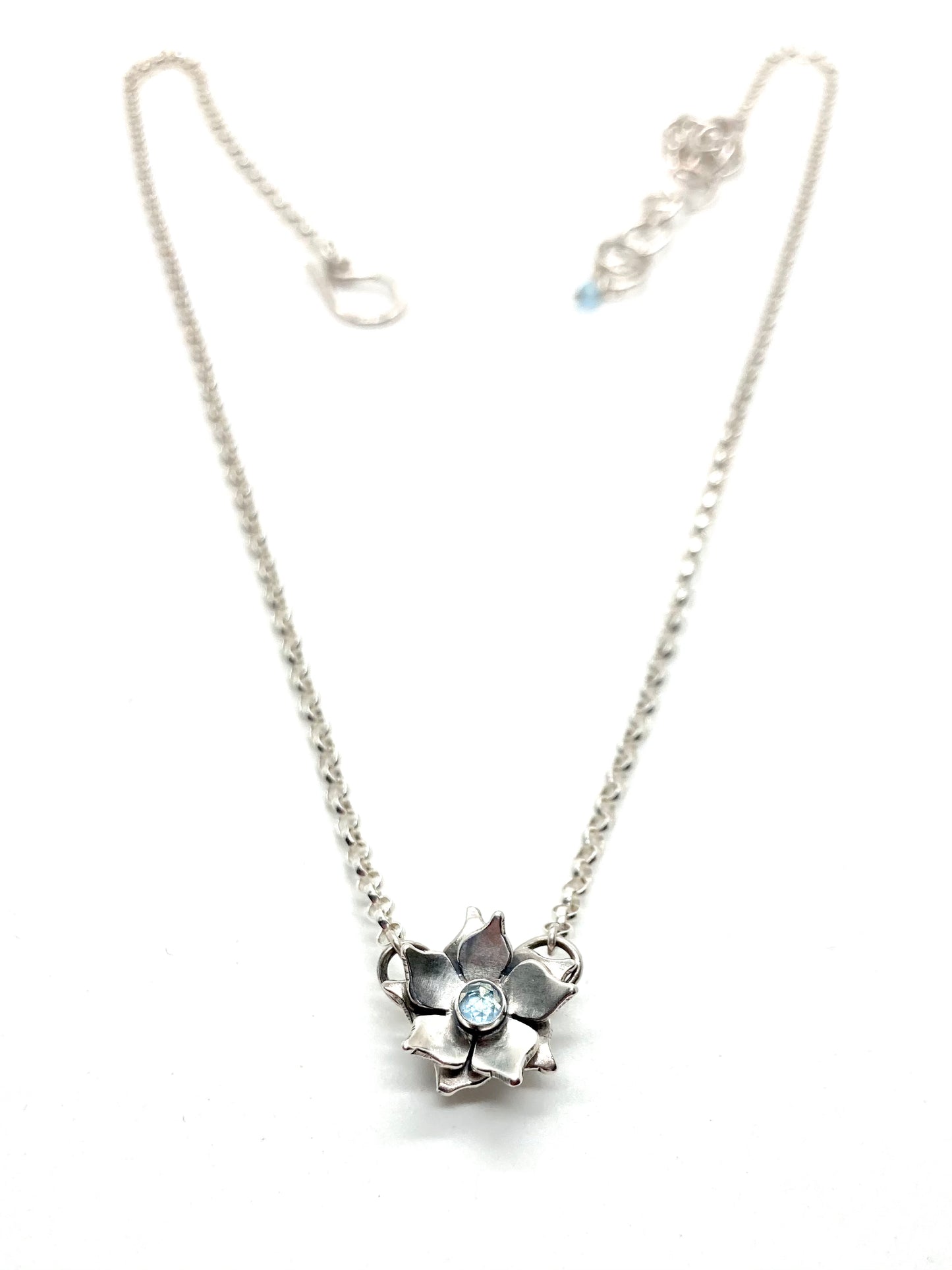 A sterling silver floral necklace with a light blue topaz gemstone at its center, attached to a chain.