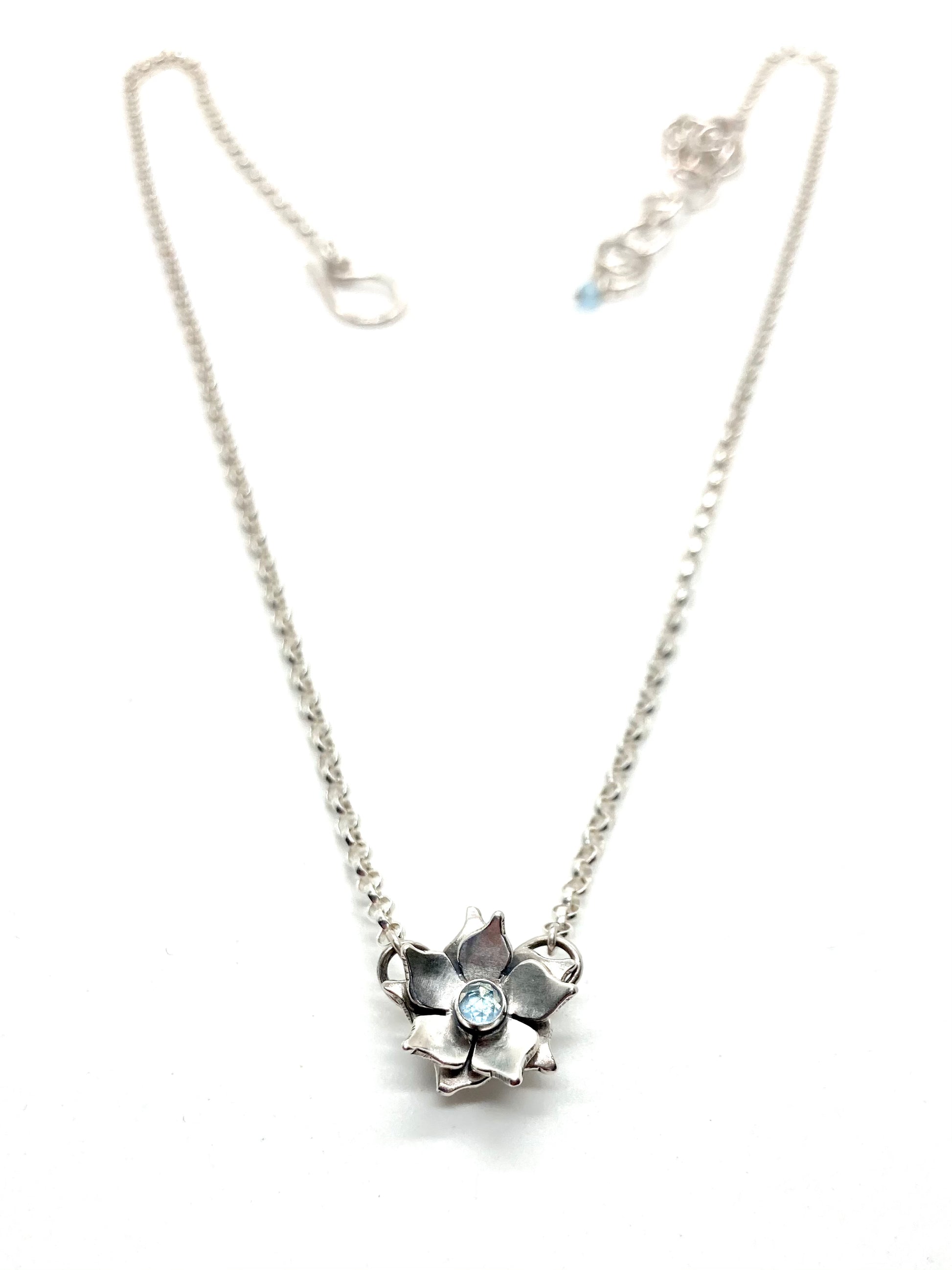 A sterling silver floral necklace with a light blue topaz gemstone at its center, attached to a chain.