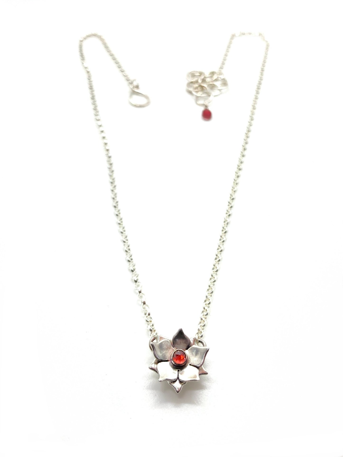 A sterling silver floral necklace with a red garnet gemstone at its center, attached to a chain.