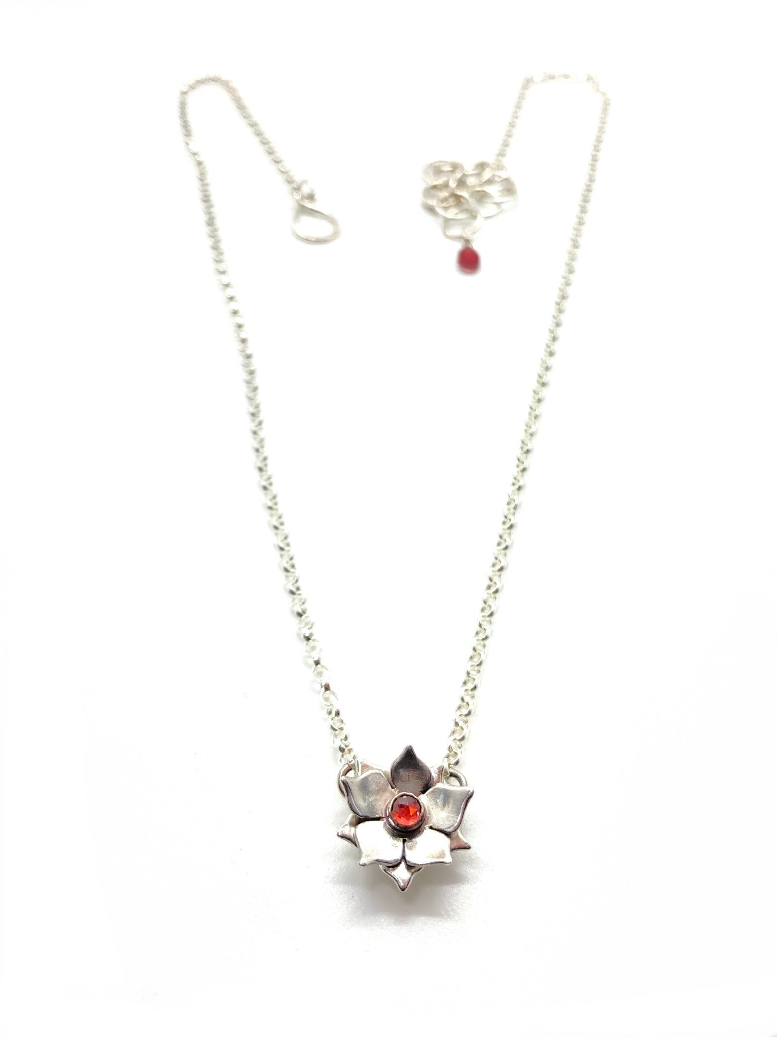 A sterling silver floral necklace with a red garnet gemstone at its center, attached to a chain.